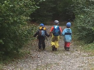 Drei Kinder mit Rucksäcken gehen einen Waldweg entlang