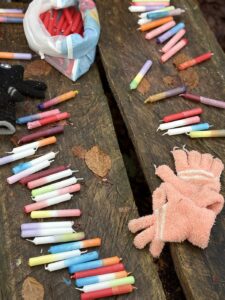 Bunte Kreidestifte und ein Paar Handschuhe liegen auf einer Holzbank