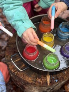 Kinderhände tunken Kreiden in Gläser mit roter, gelber, grüner und blauer Farbe
