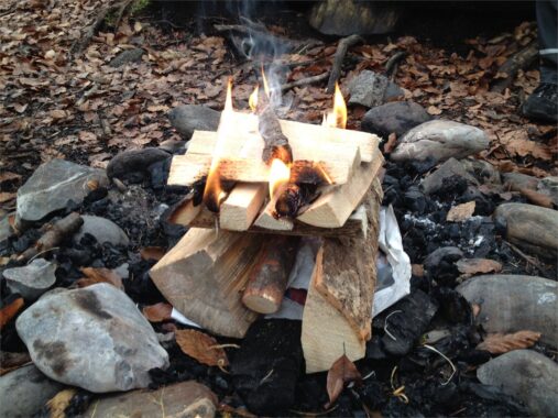 Ein Feuer brennt zwischen Holzscheiten in einer Feuerstelle aus Steinen
