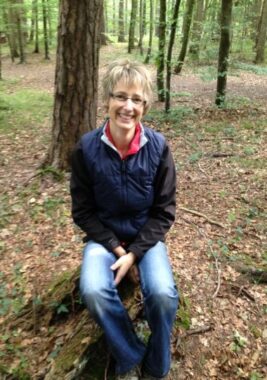 Eine Betreuerin sitzt auf einem Baumstrunk im Wald