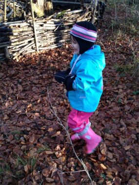 Ein Kind in türkiser Jacke geht mit einem Stock durchs Laub