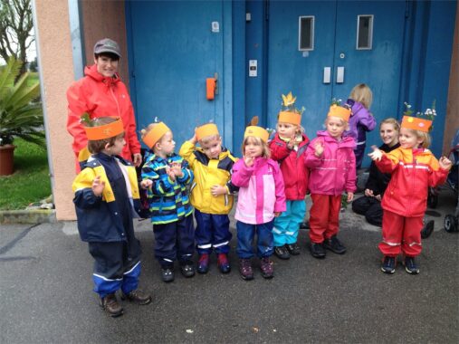 Eine Kindergruppe mit Papierkronen steht vor einer blauen Tür