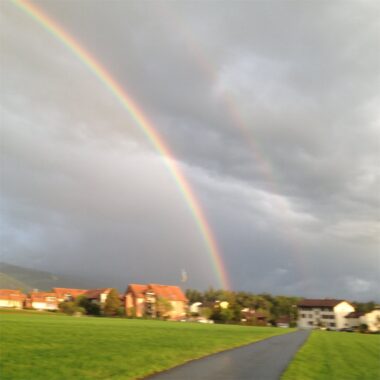 Ein Regenbogen über Wiesen und Häusern am Abend