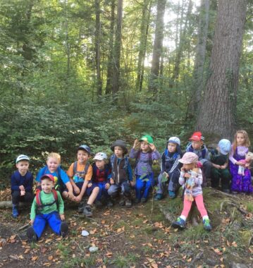 Eine Kindergruppe sitzt für ein Gruppenbild am Waldboden