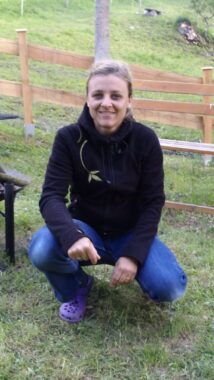 Eine Betreuerin kniet auf einer Wiese neben einem Holzzaun