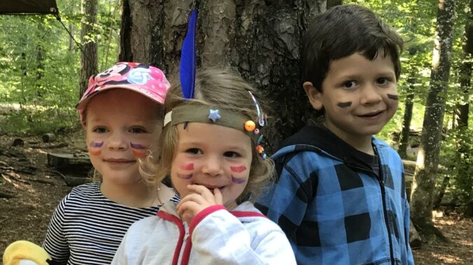 Drei Kinder mit bemalten Gesichtern stehen nebeneinander im Wald