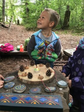 Ein Kind schaut über einen Tisch mit Steinen und Tannzapfen nach oben
