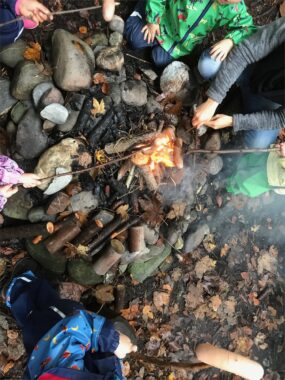 Kinder braten Würste an Stöcken über dem Feuer