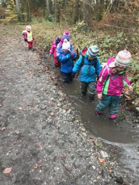 Eine Kinderreihe geht dem nassen Waldweg entlang
