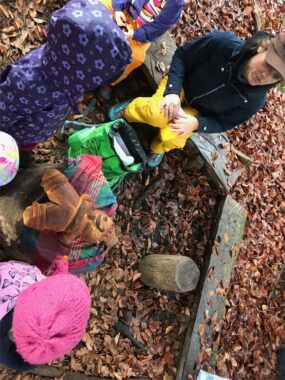 Eine Betreuerin und Kinder basteln am Waldboden