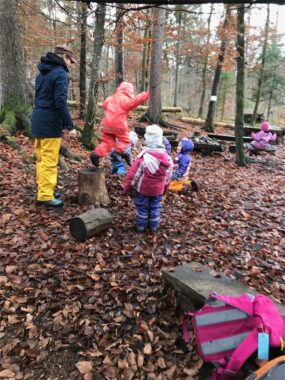 Eine Betreuerin spielt mit Kindern zwischen den Bäumen