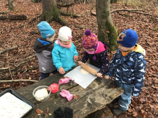 Kinder wallen Teig auf einem Holztisch im Wald aus