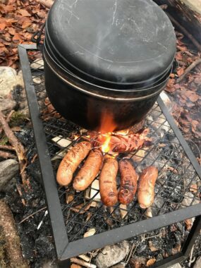 Ein Topf und Würste garen über dem Feuer