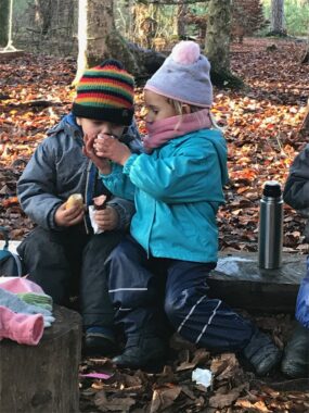 Zwei Kinder essen ihren Znüni auf einem Baumstrunk
