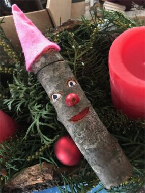 Eine bemalte Holzfigur mit Filzmütze liegt auf Tannenzweigen