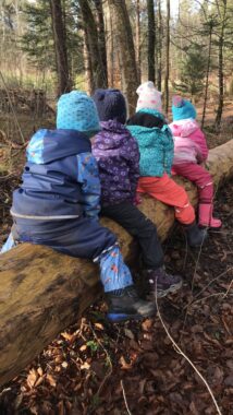 Kinder sitzen nebeneinander auf einem liegenden Baumstamm