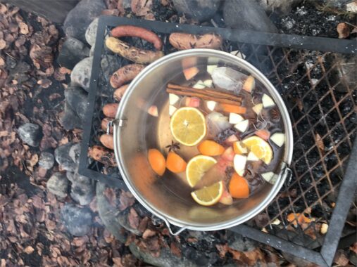 Punsch mit Orangenscheiben und Gewürzen kocht im Topf über dem Feuer