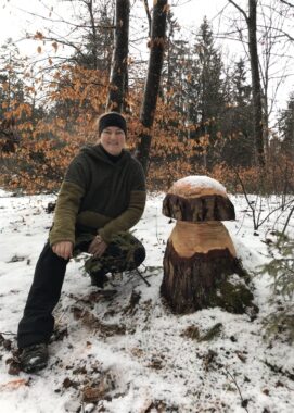 Eine Person in grüner Jacke kniet im Schnee neben der Pilzskulptur