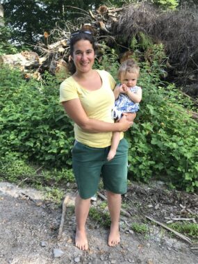 Eine Betreuerin barfuss auf dem Waldweg mit einem Kleinkind auf dem Arm