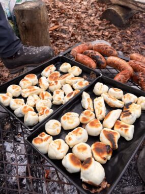 Bleche mit gebackenen Brötchen und Würsten an der Feuerstelle