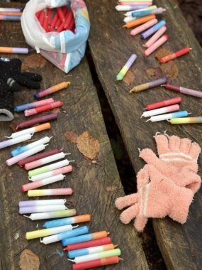 Bunte Kreidestifte und ein Paar Handschuhe liegen auf einer Holzbank