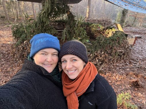 Zwei Betreuerinnen in Winterjacken lachen im Wald in die Kamera