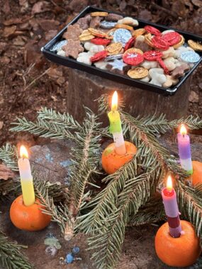 Blech mit bunt verzierten Guetzli neben brennenden Kerzen in Orangenschalen
